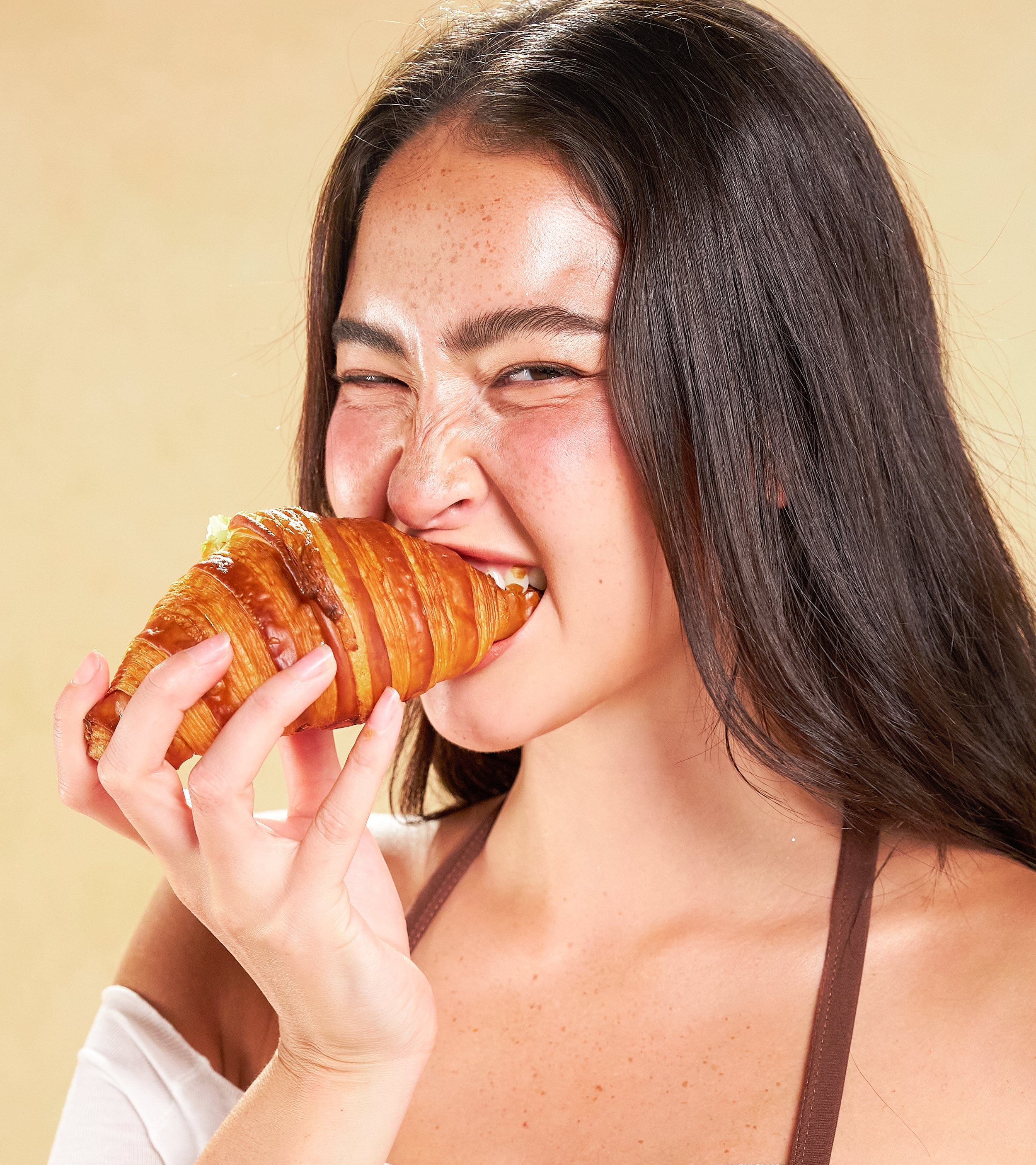 Woman in a brown SARIE bra smiling while biting a croissant